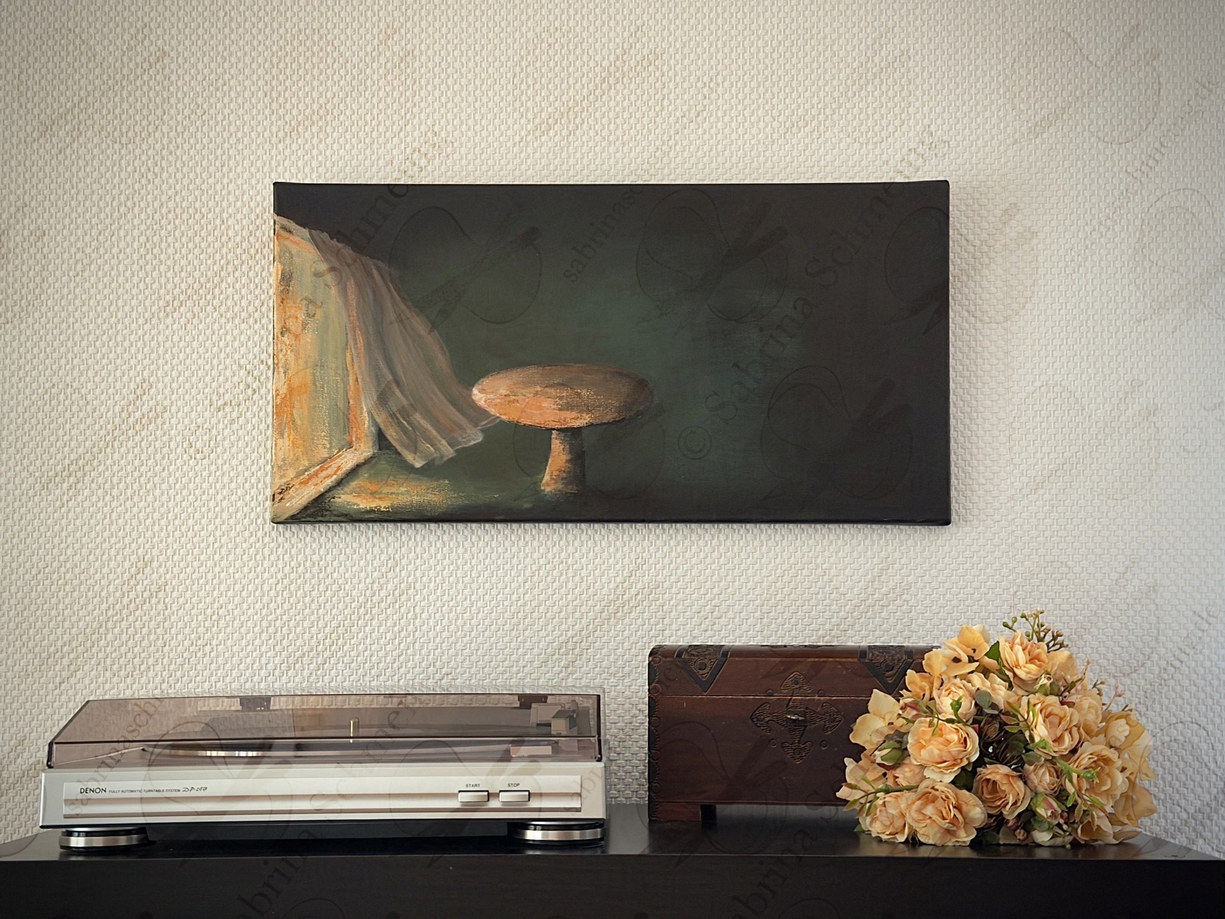 Kunstwerk "Der leere Tisch" von Sabrina Schmeing © 2026. Ansicht des Werks an einer Wand in einem Wohnzimmer.